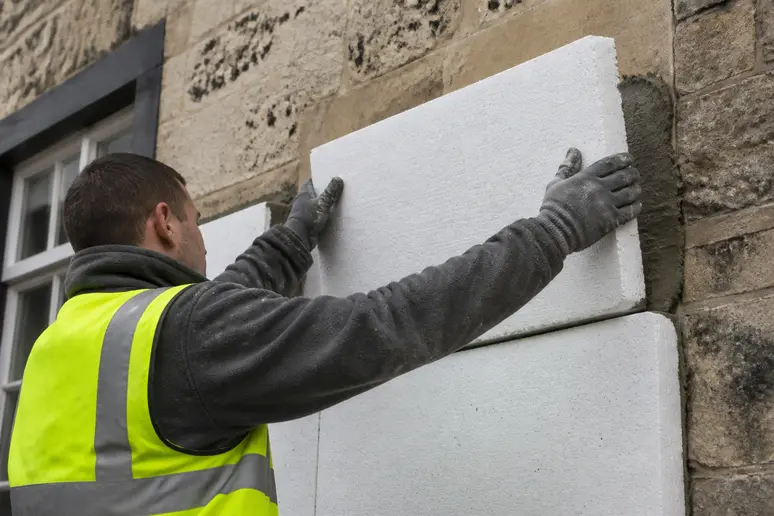 Ouvrier posant des panneaux d'isolation sur la façade d'un logement ancien