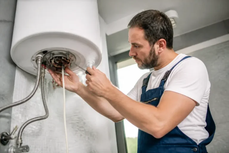 Un plombier installe une résistance chauffe-eau dans un local technique bien éclairé.
