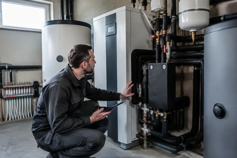 Technicien vérifiant une installation de pompe à chaleur géothermique dans un local technique résidentiel.