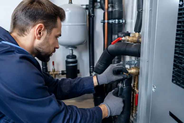 Technicien effectuant les raccordements hydrauliques d'une pompe à chaleur air-eau dans un local technique