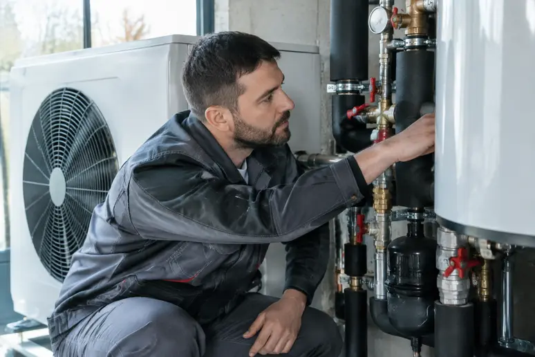Technicien vérifiant les raccordements hydrauliques d'une pompe à chaleur dans une chaufferie.